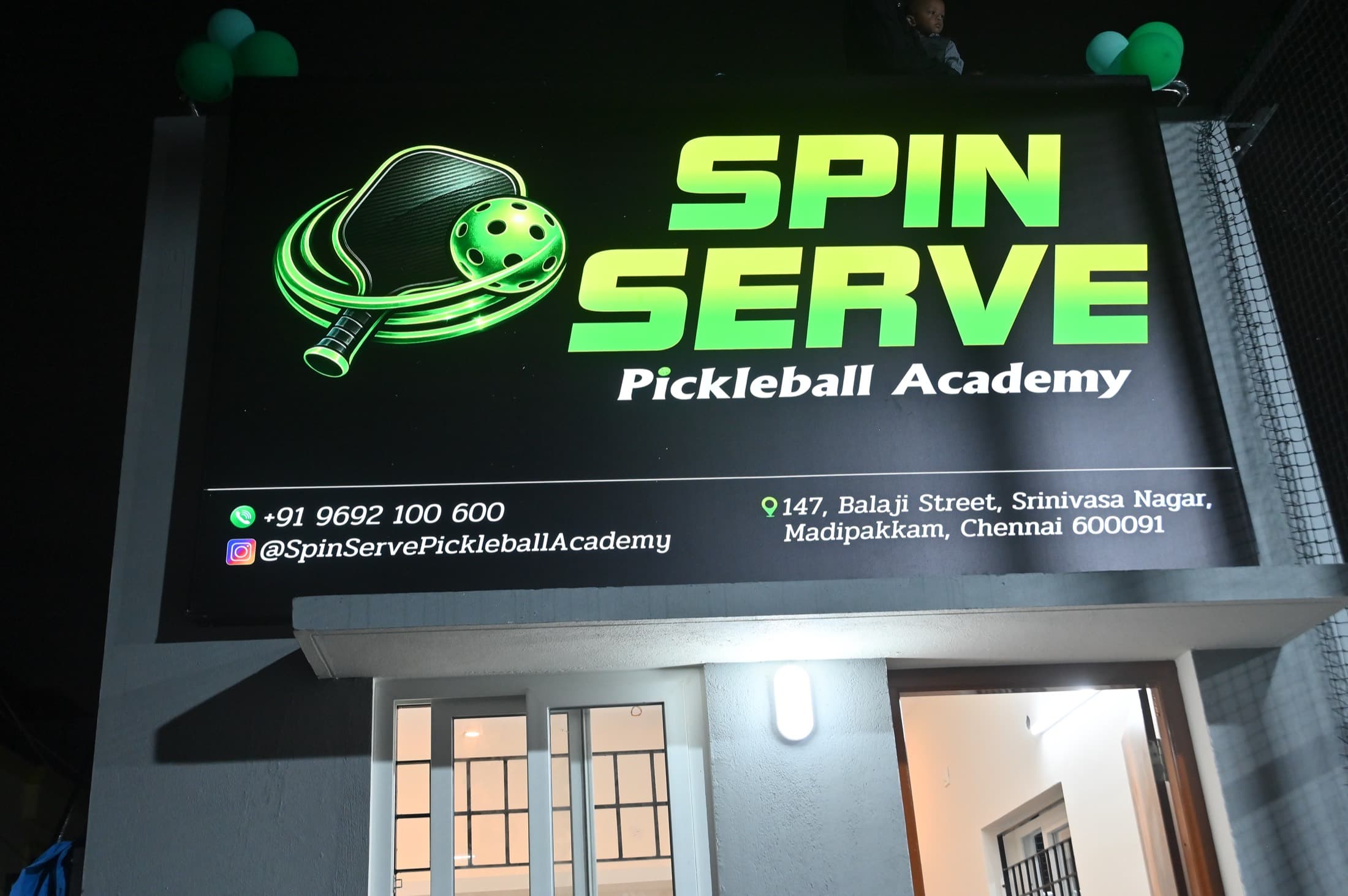 The lit Spin Serve signboard above the entrance after dark