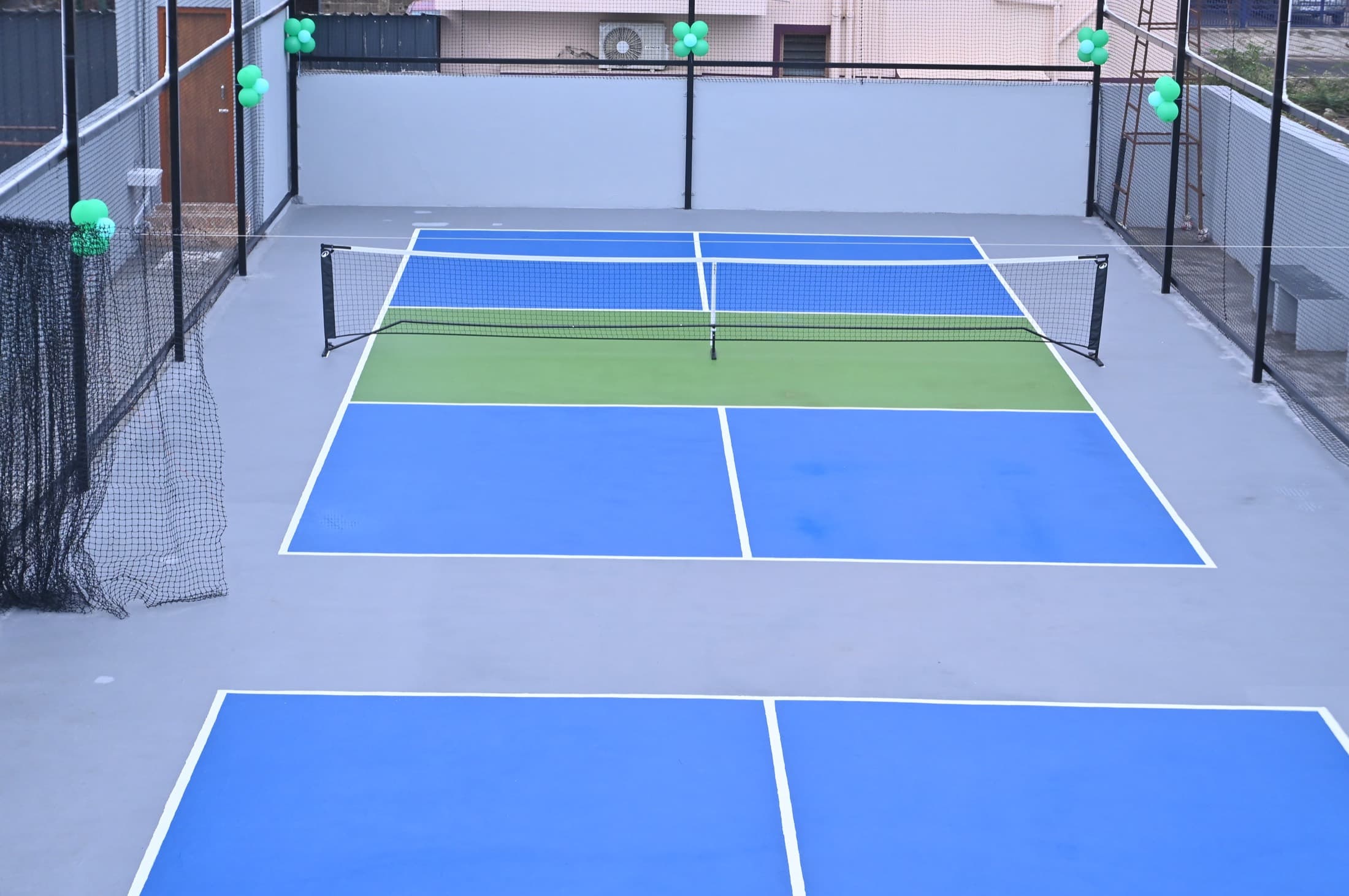 Both pickleball courts at Spin Serve seen from the near baseline, blue and green acrylic surfaces with the nets up